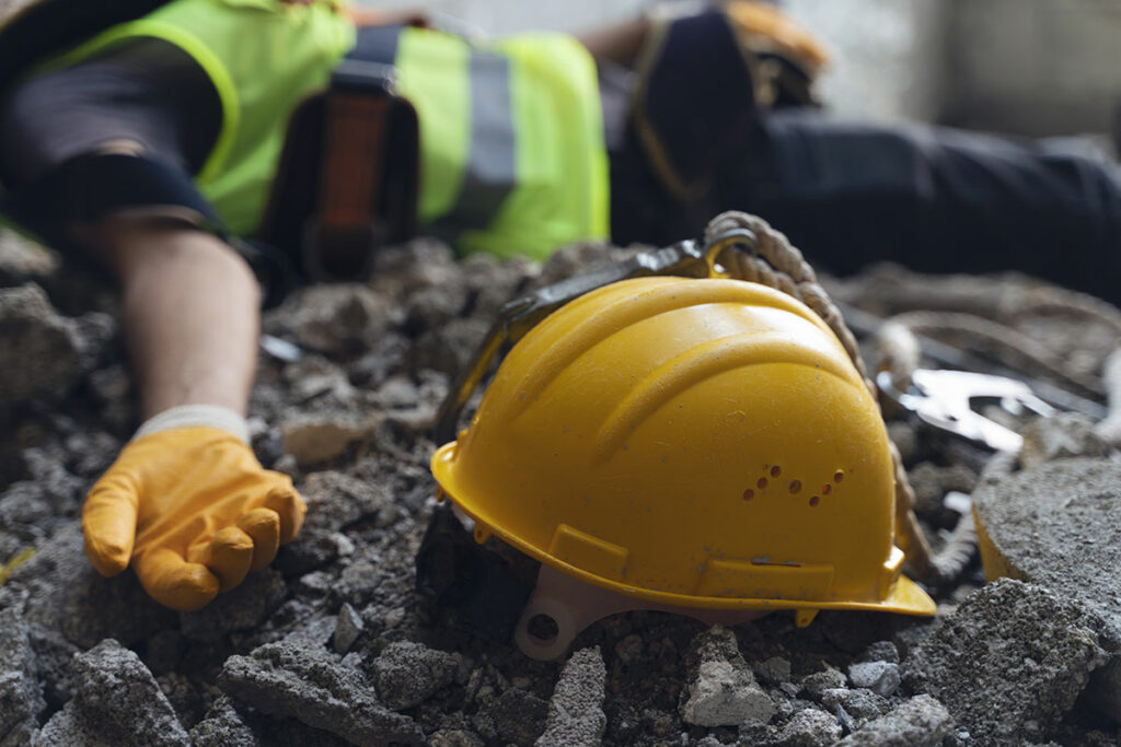 an injured lone worker laying on the ground with a hard hat next to him